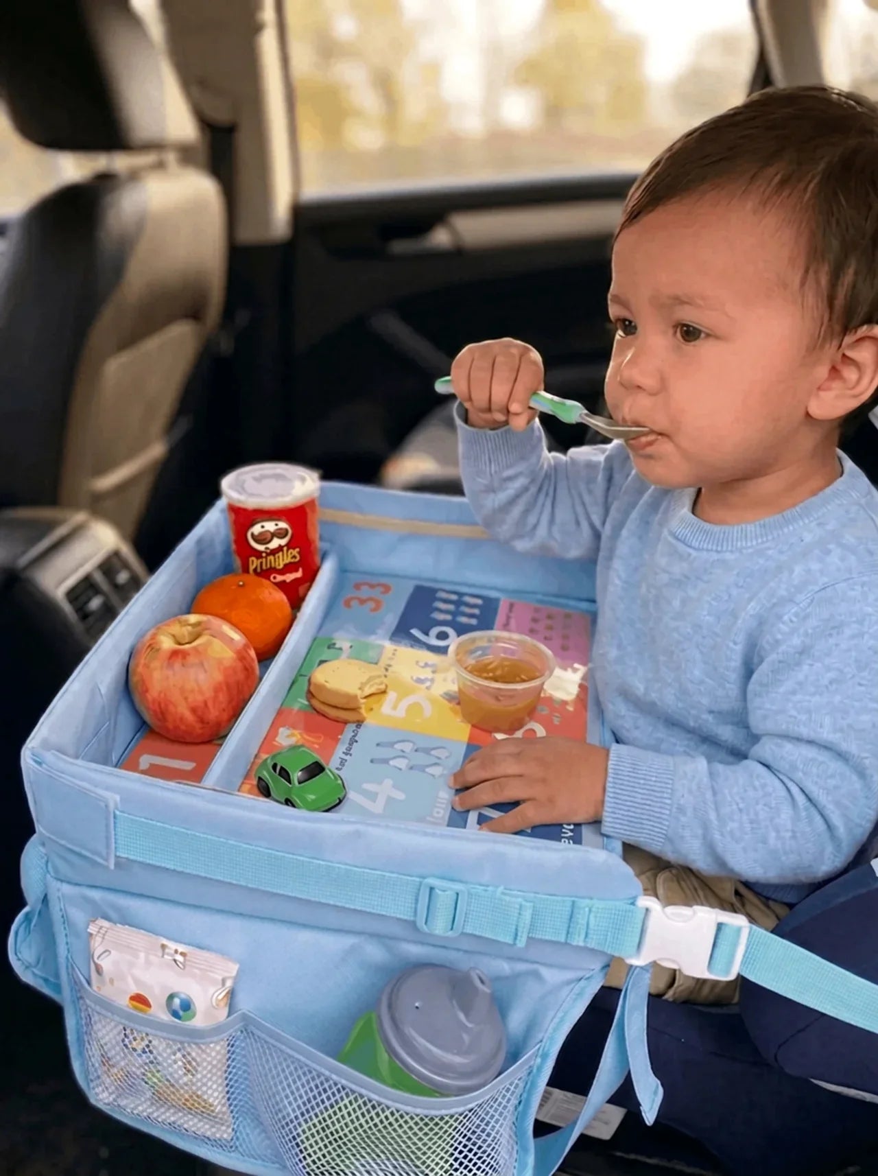 Child in a car seat using the blue Little Rider Travel Tray
